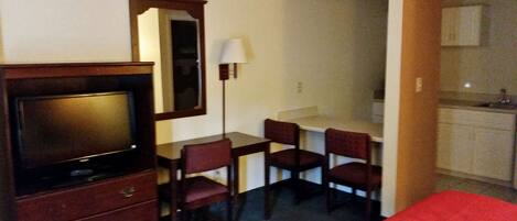 Ein Hotelzimmer mit Fernseher, Schreibtisch mit Stühlen, Spiegel und Küchenzeile.