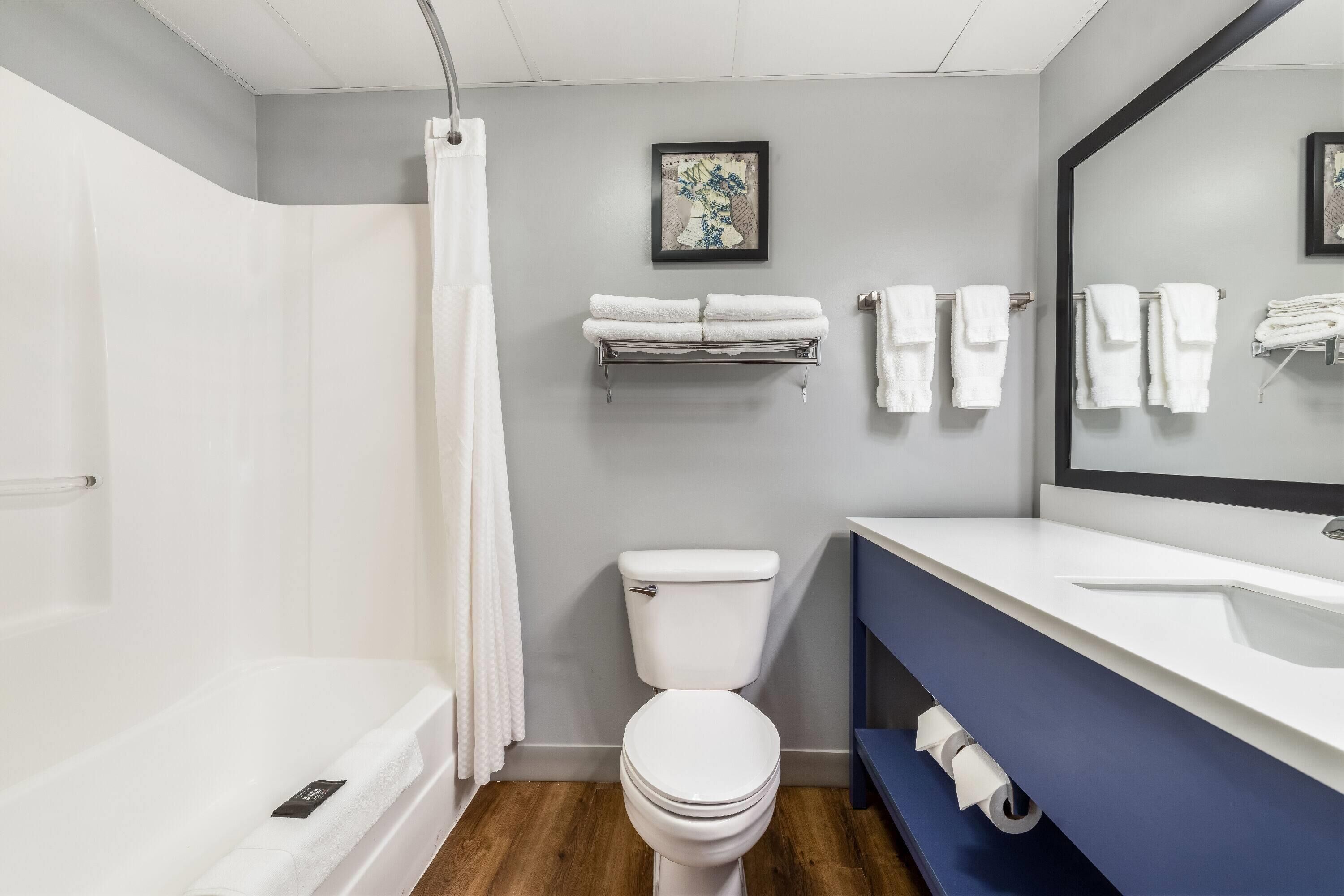 Et moderne badeværelse med et hvidt badekar, et toilet og en blå kommode.