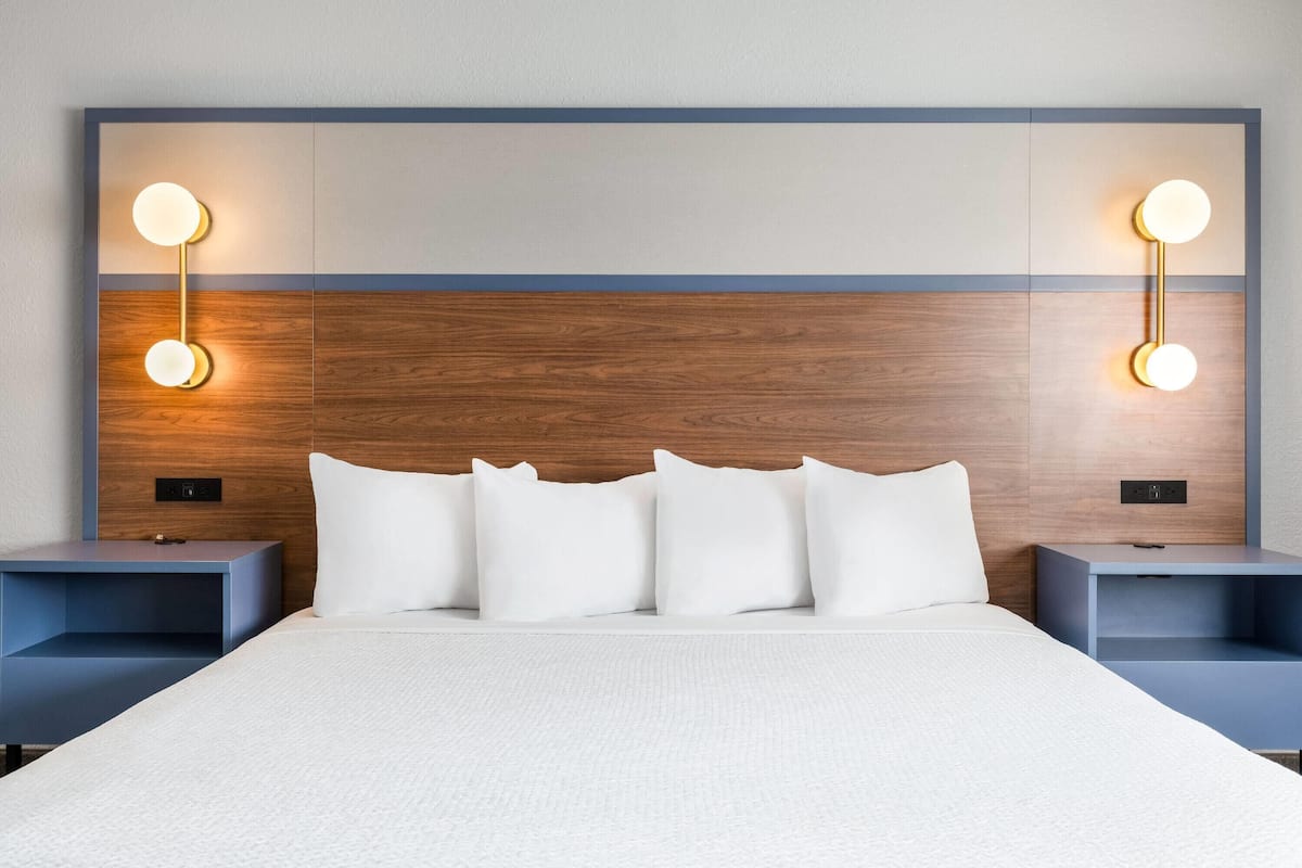 A modern hotel room with a large bed, two bedside tables, and wall-mounted reading lights.