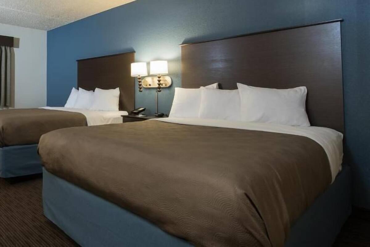 A hotel room with two beds, a nightstand, a lamp, and a window with curtains.