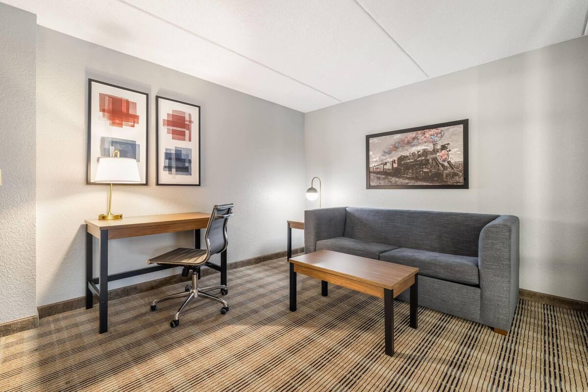 A modern room with a desk, office chair, sofa, and a framed picture of a train.