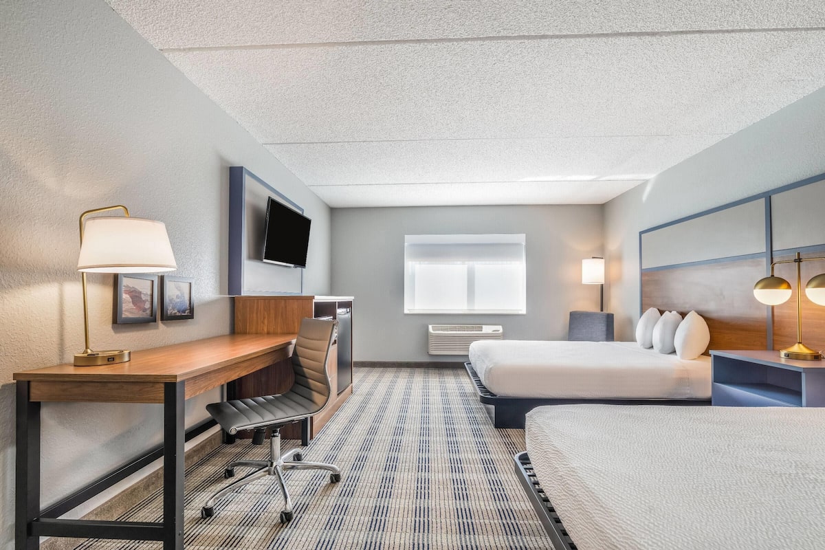 A hotel room with a bed, desk, chair, and a TV mounted on the wall.