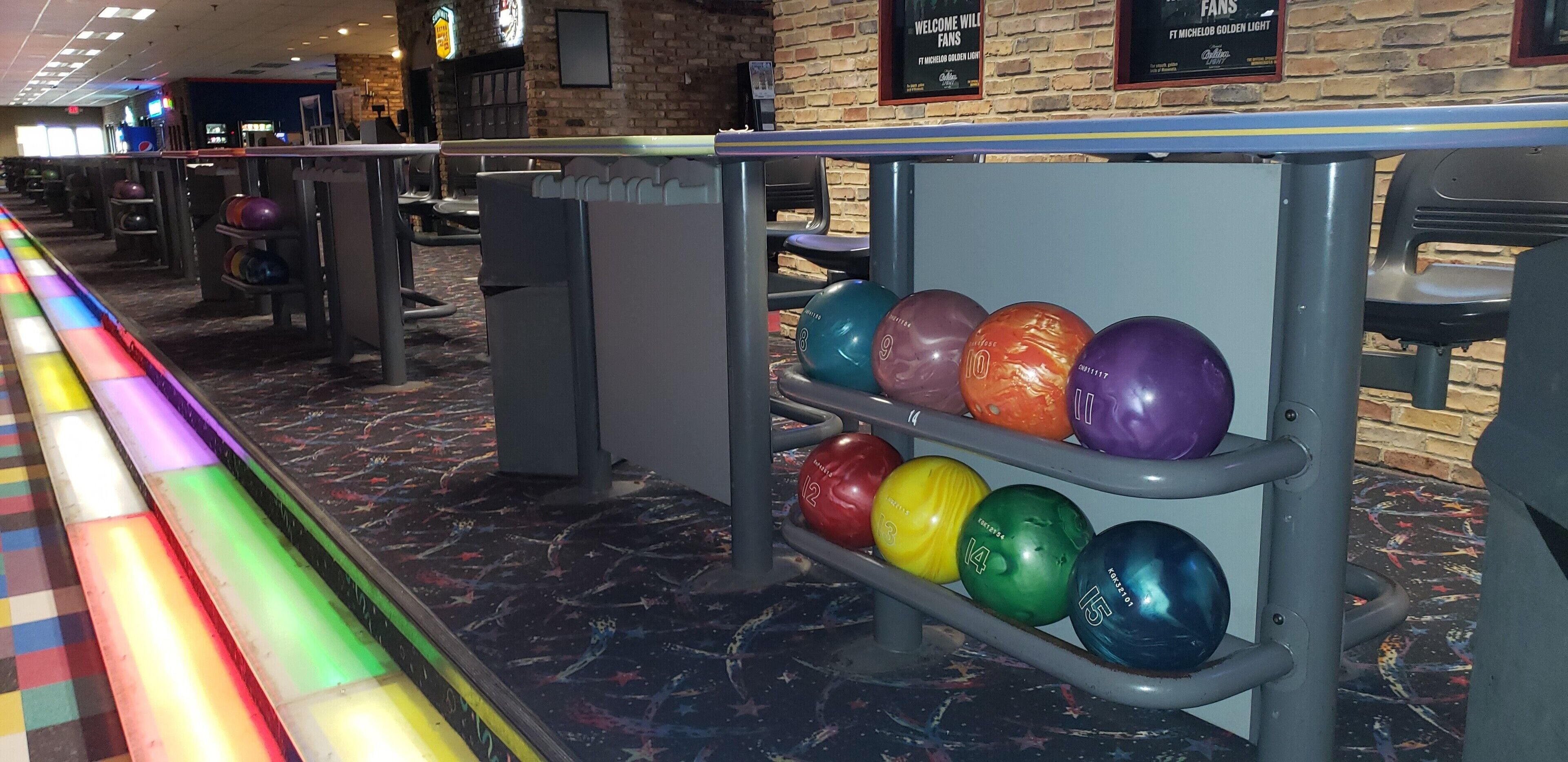 Une salle de bowling où l’on trouve une variété de boules de bowling colorées, disposées sur des présentoirs.