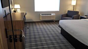 A hotel room with a bed, a desk, a chair, a TV, and a window with blinds.