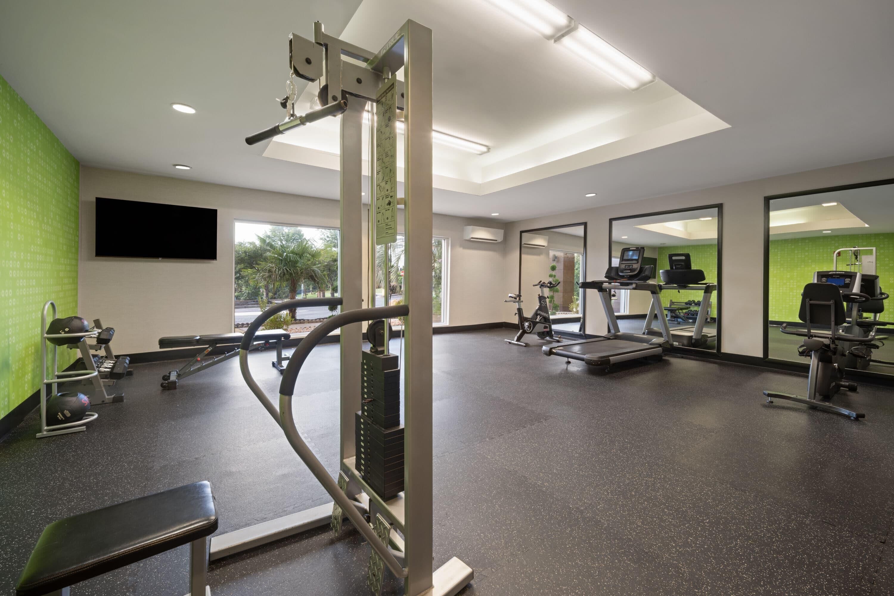 Un gimnasio con equipo de ejercicio, una banca y un espejo grande.