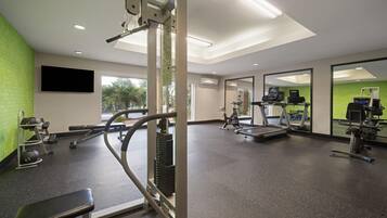 Un gimnasio con equipo de ejercicio, una banca y un espejo grande.