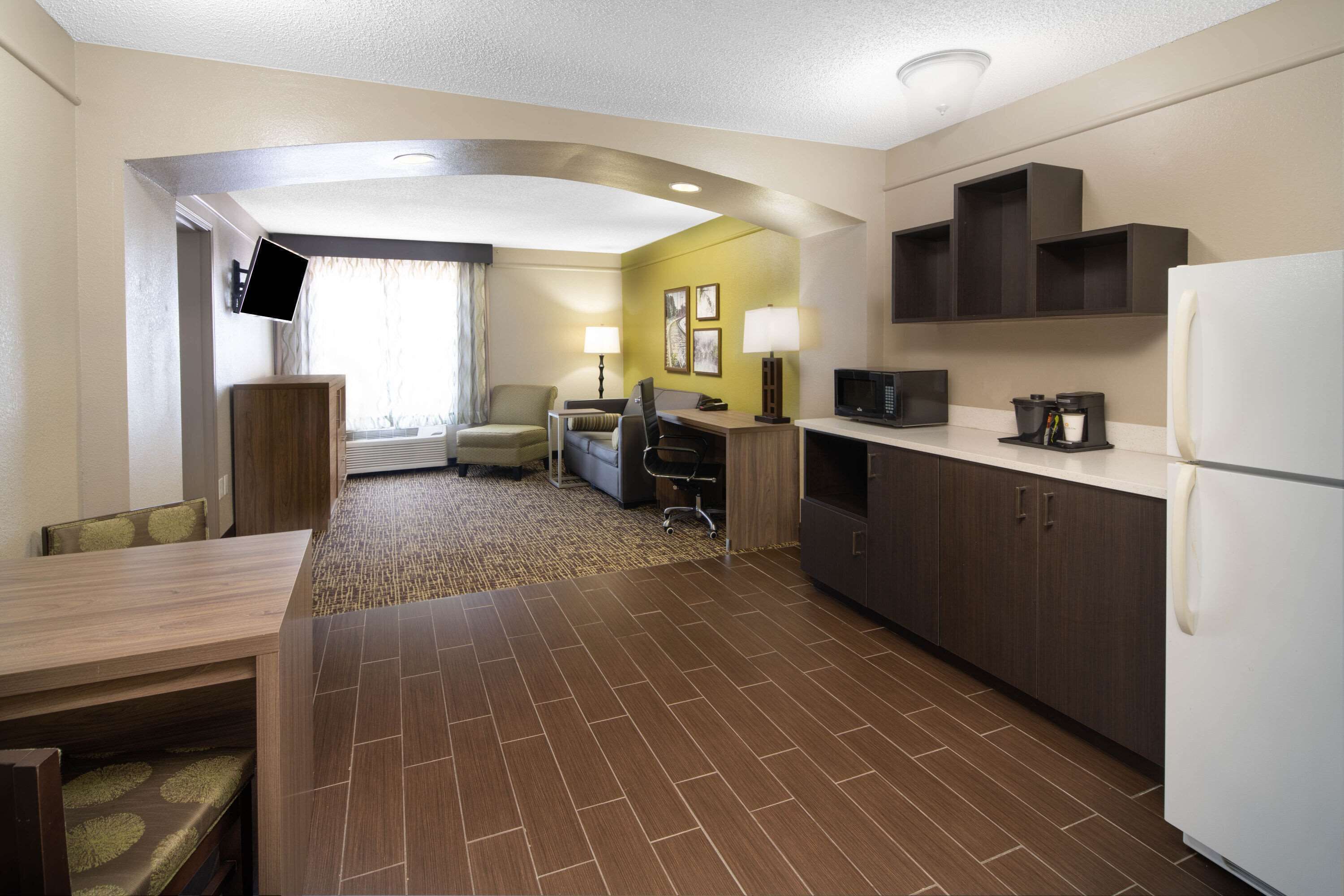 A hotel room with a dining area, kitchenette, and a TV mounted on the wall.