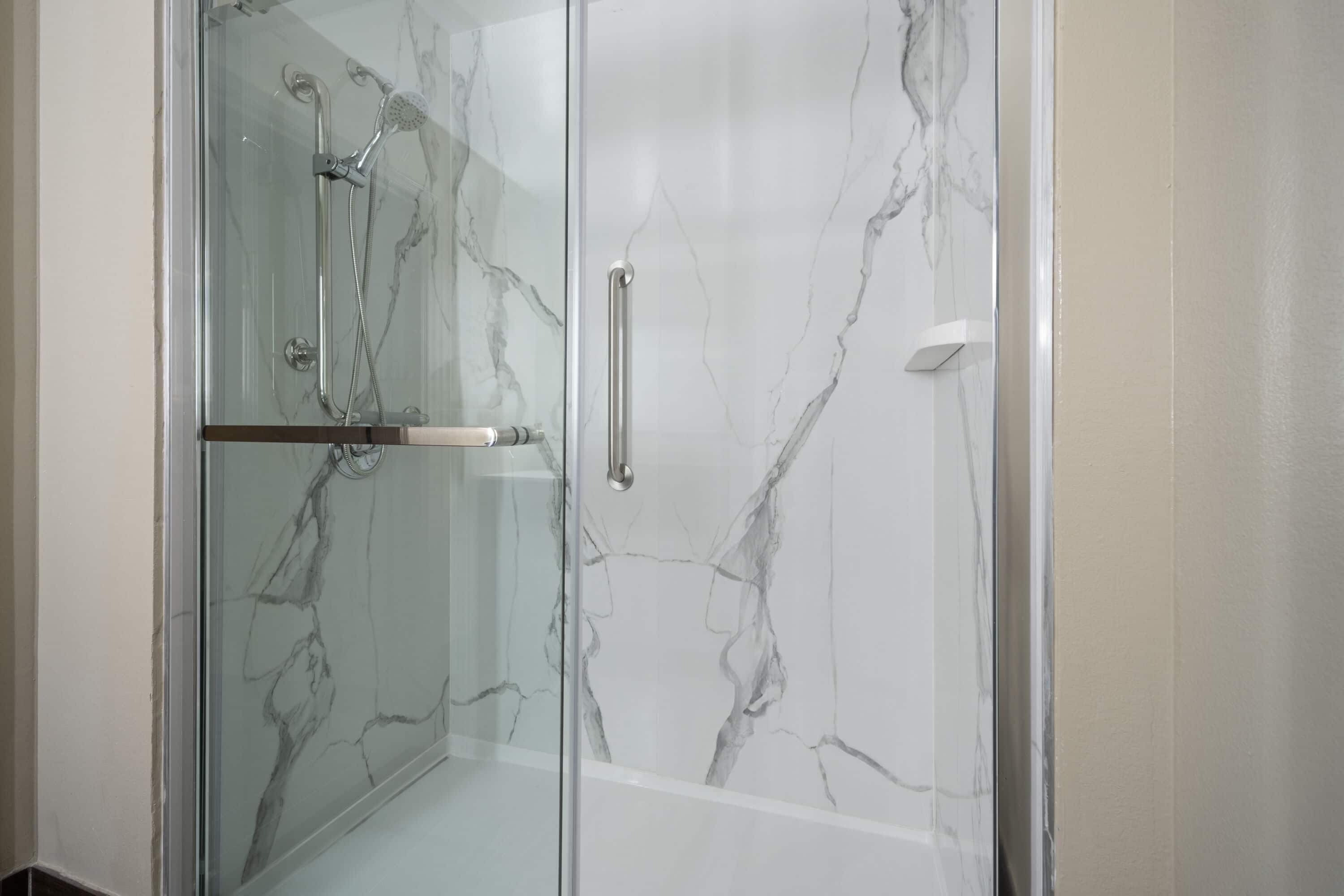 Eine begehbare, gläserne Dusche mit Marmordesign, einem Türgriff und einer Duschbrause.