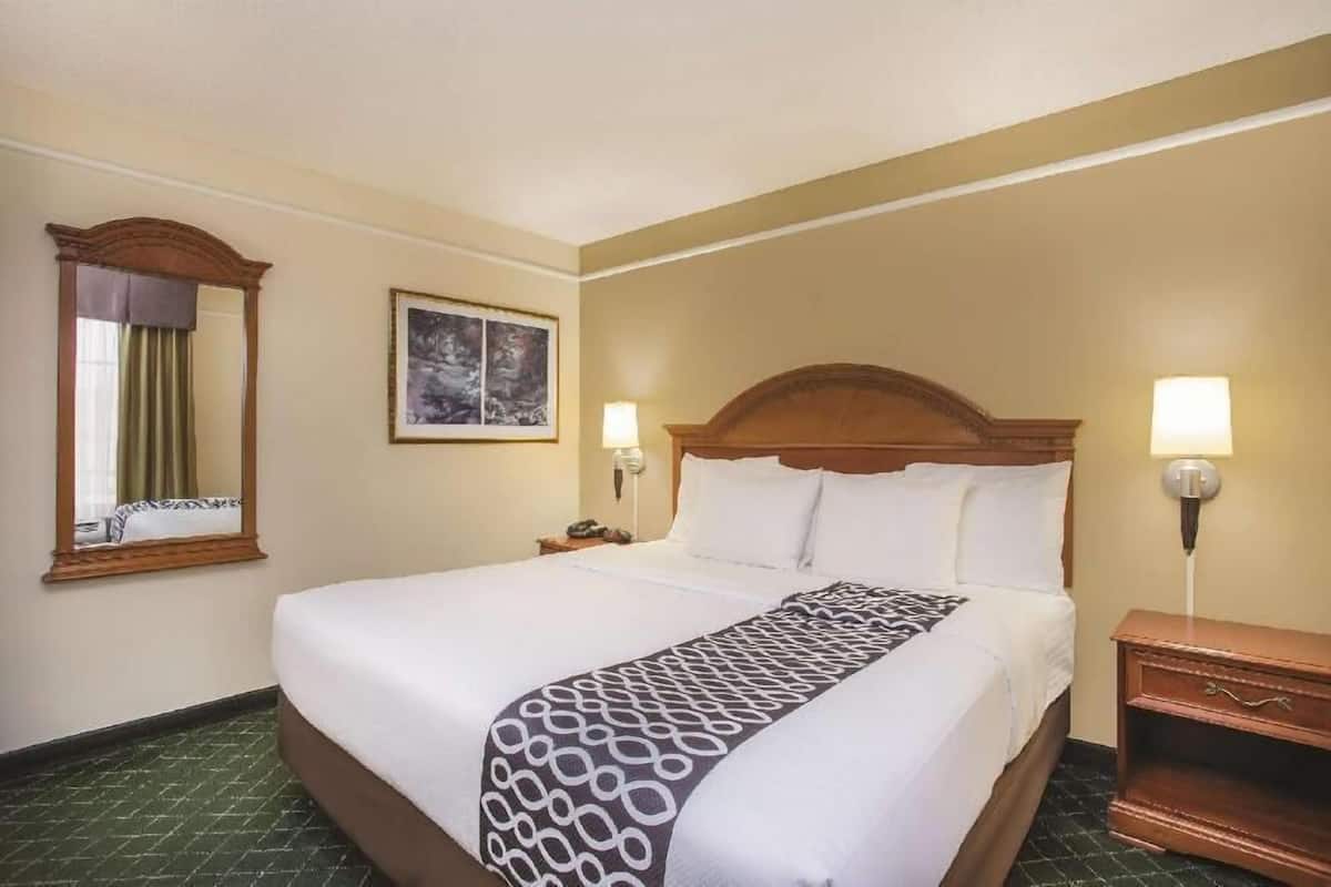 Ein Hotelzimmer mit einem großen Bett, zwei Nachttischlampen, einem Nachttisch, einem Spiegel und einem gerahmten Bild an der Wand.
