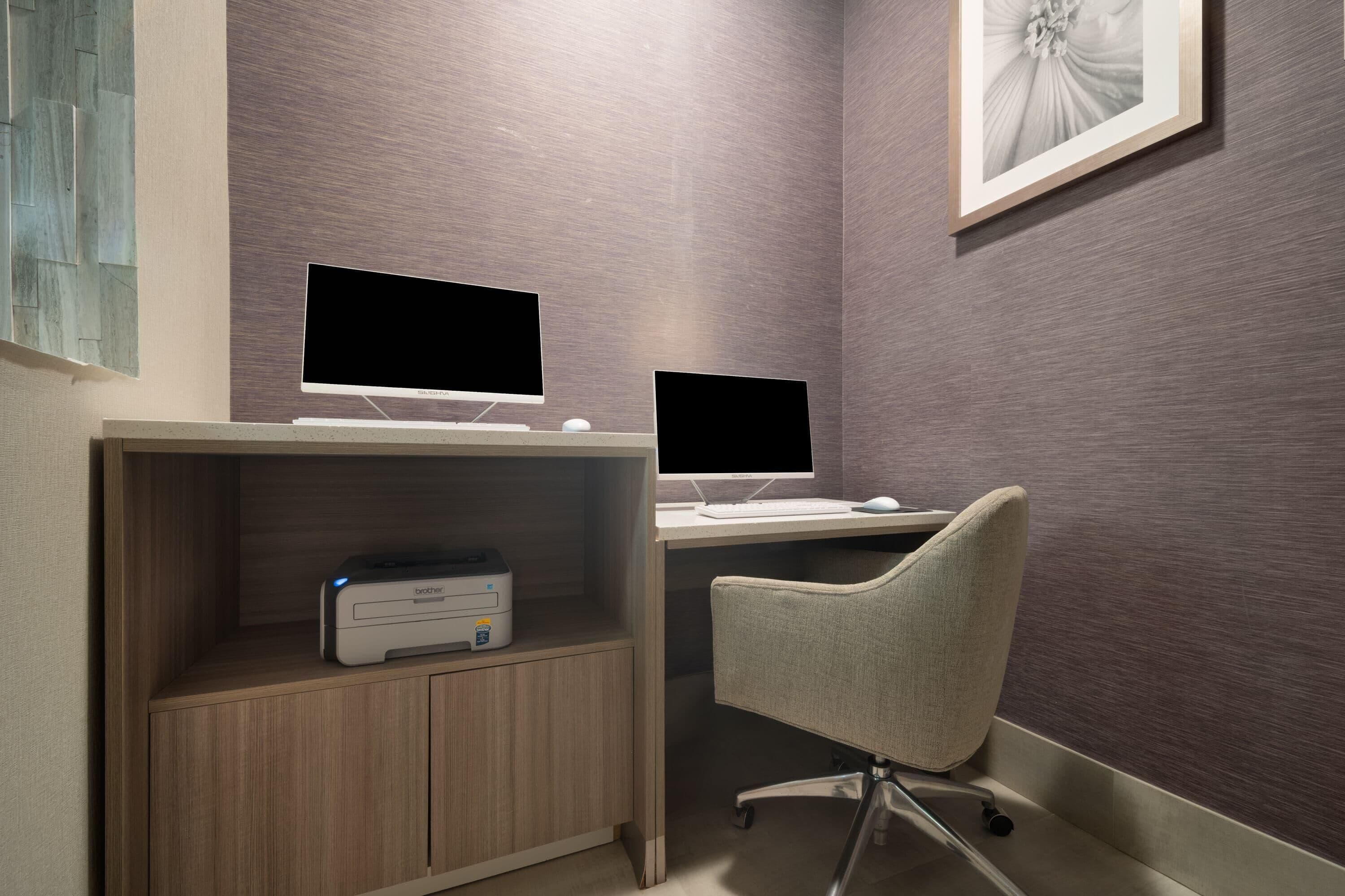 A workspace with two computer monitors, a printer, and a chair.