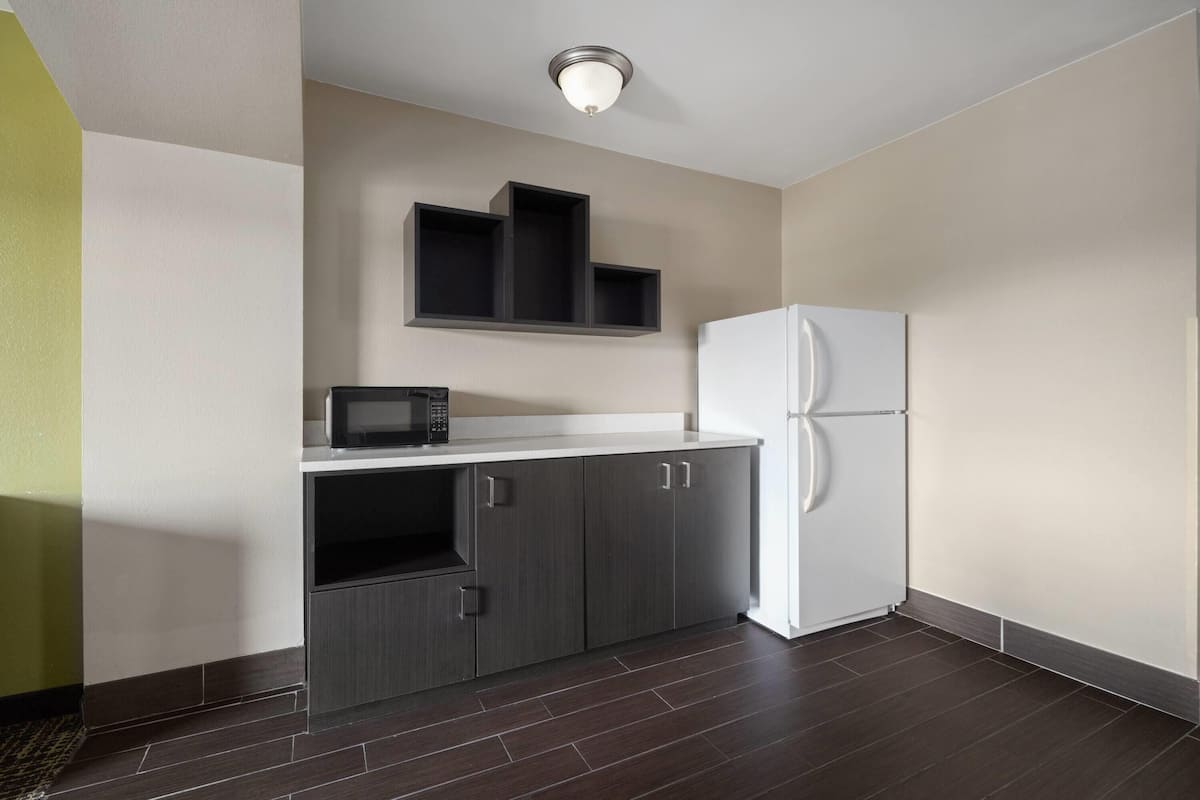 A modern kitchen with dark cabinetry, a white refrigerator, and a microwave on a white countertop.
