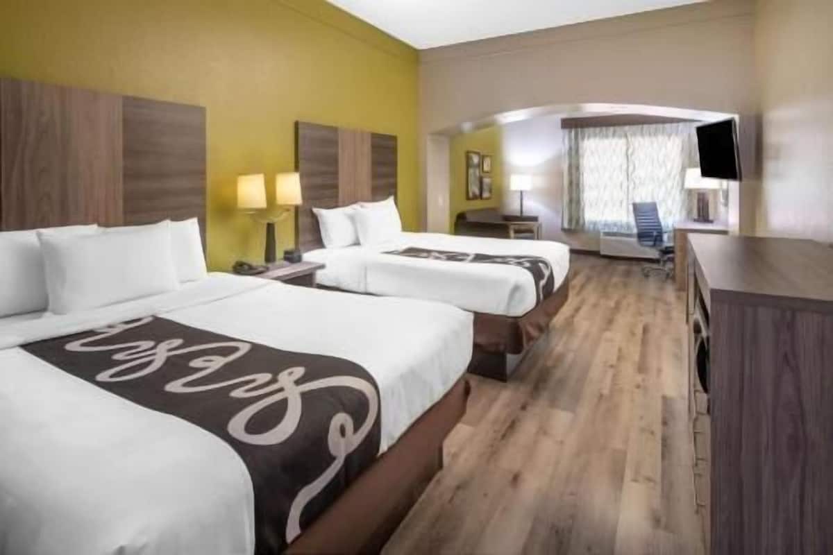 Ein Hotelzimmer mit zwei Betten, einem Schreibtisch, einem Stuhl und einem Fernseher.