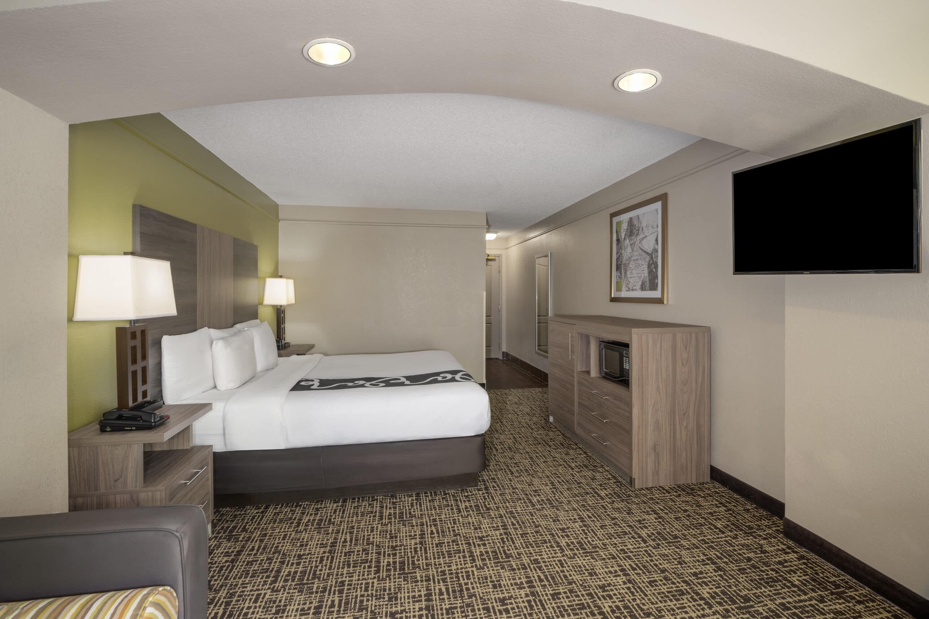 Een hotelkamer met een bed, nachtlampjes, een flatscreen televisie, een spiegel en een klein bureau met een lamp.