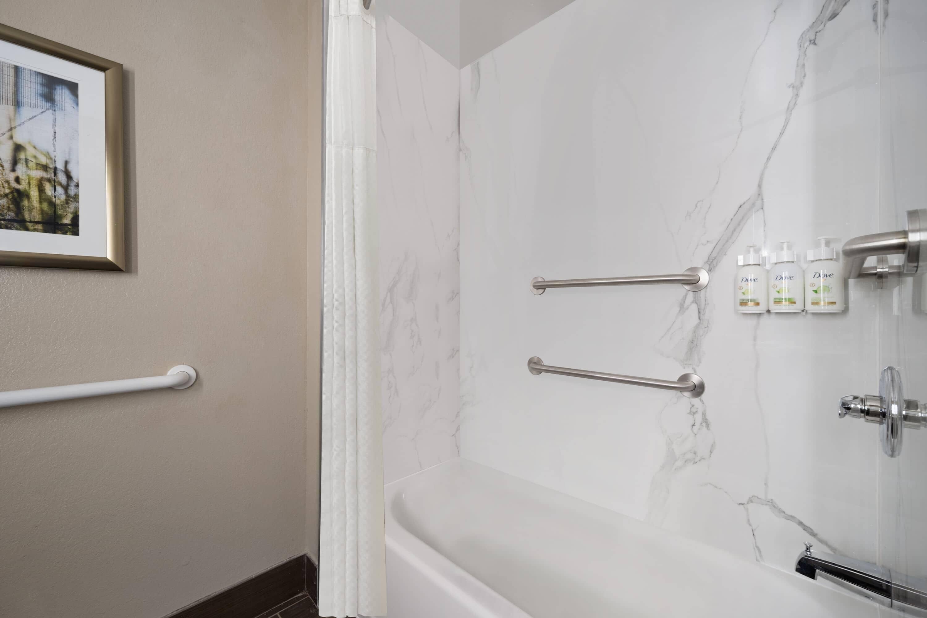 Un baño con paredes de mármol, una bañera y barras de apoyo.