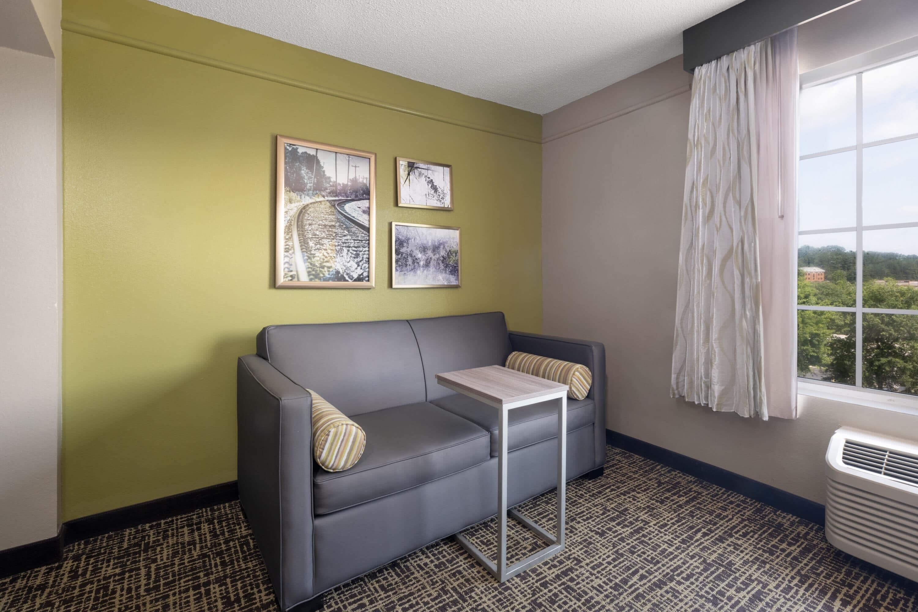 A room with a grey sofa, a small table, and three framed pictures on the wall.