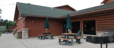 A wooden cabin with a patio area featuring picnic tables and umbrellas.