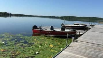 A calm lake with a wooden dock and a red boat docked at the pier.