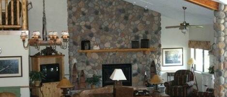 A cozy living room with a stone fireplace, wooden beams, and a ceiling fan.