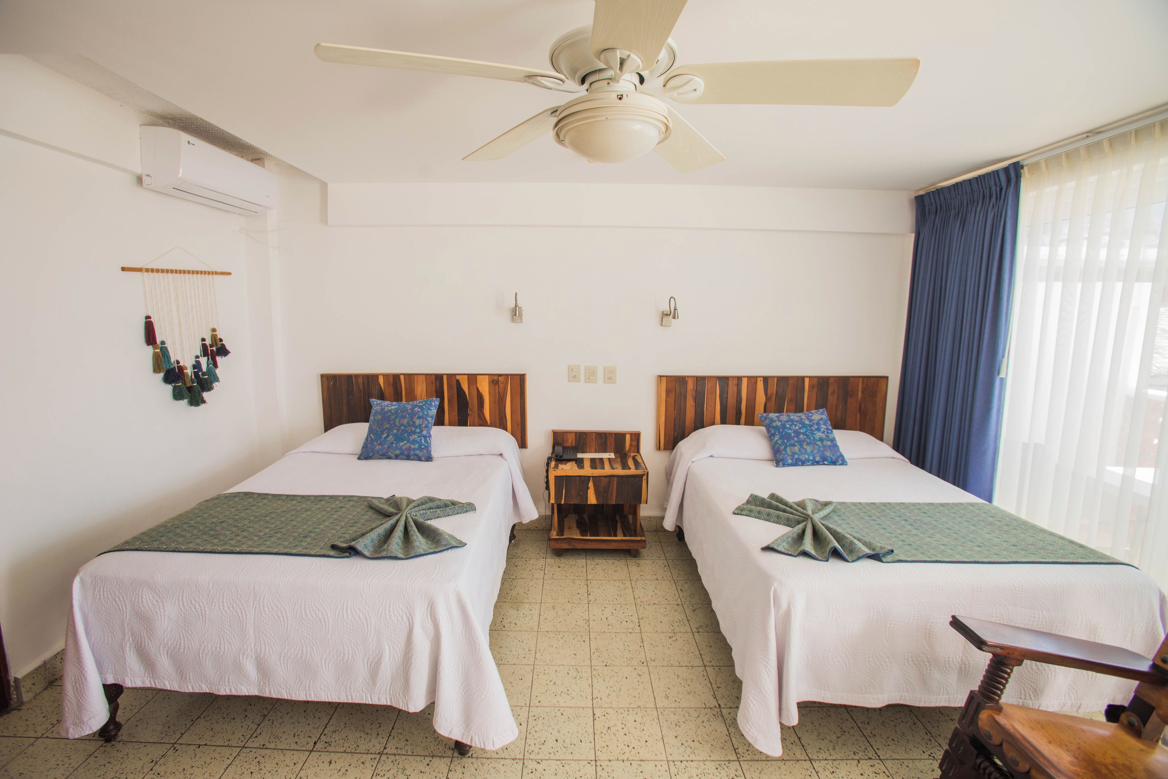 A hotel room with two beds, a ceiling fan, a wall-mounted phone, and a small wooden nightstand.