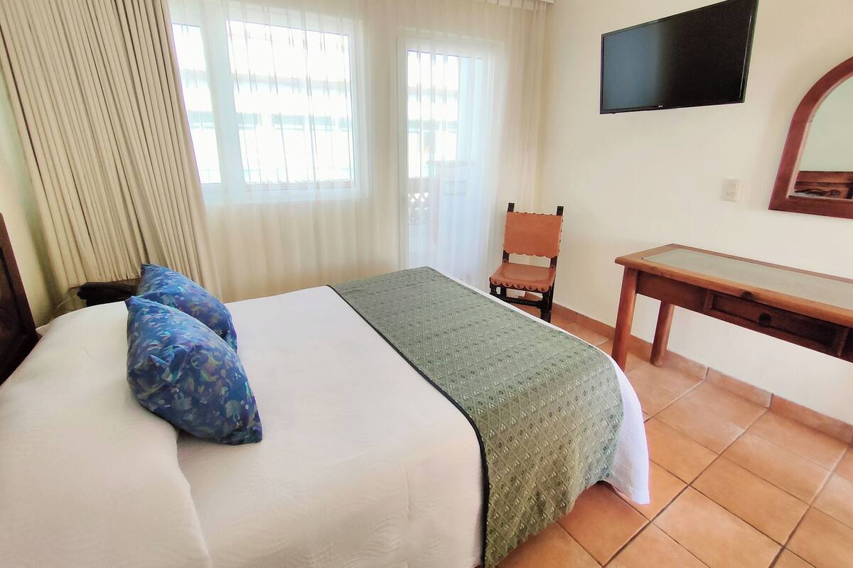 Ein Hotelzimmer mit Bett, Schreibtisch, Stuhl, Fernseher und einem Fenster mit Vorhängen.