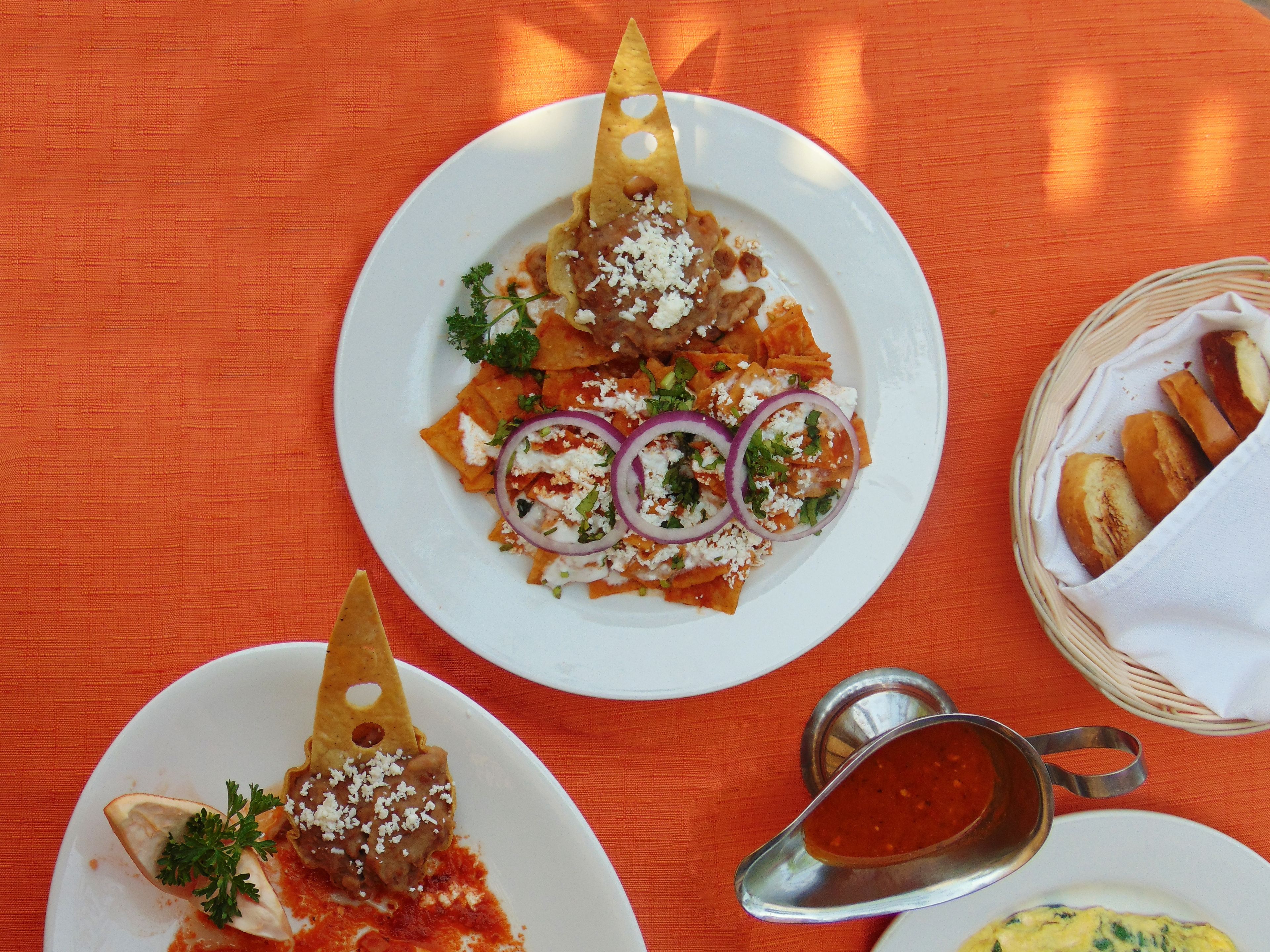 A table with two plates of food, one with nachos and the other with a different dish, and a basket of bread.