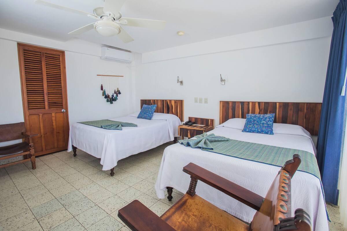 Ein Hotelzimmer mit zwei Betten, einer Holzbank, einem Deckenventilator und einem Holzschrank.
