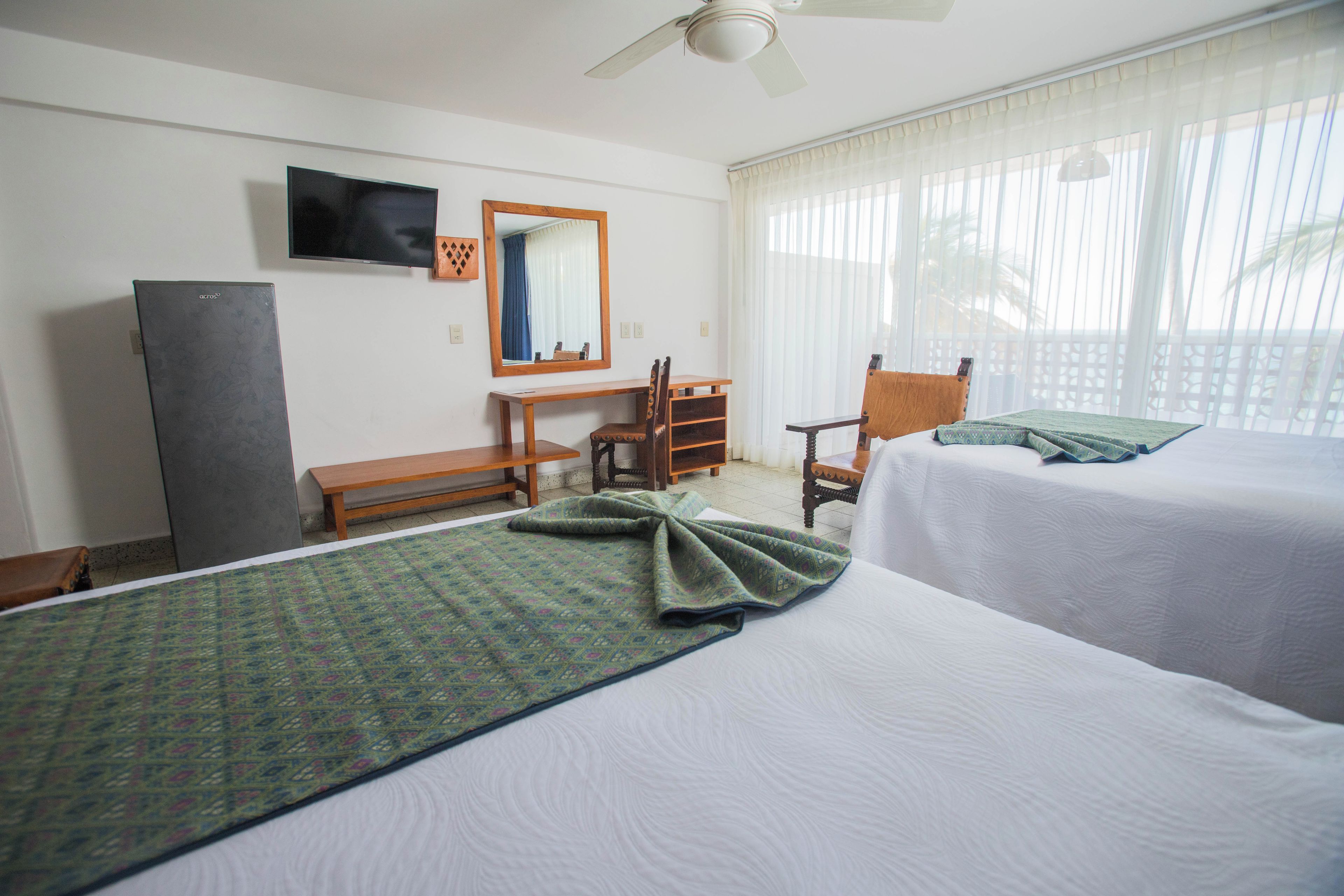 A hotel room with two beds, a desk, a chair, a television, and a window with curtains.