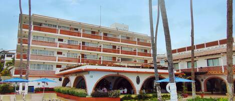 A hotel with a swimming pool, outdoor seating, and palm trees.
