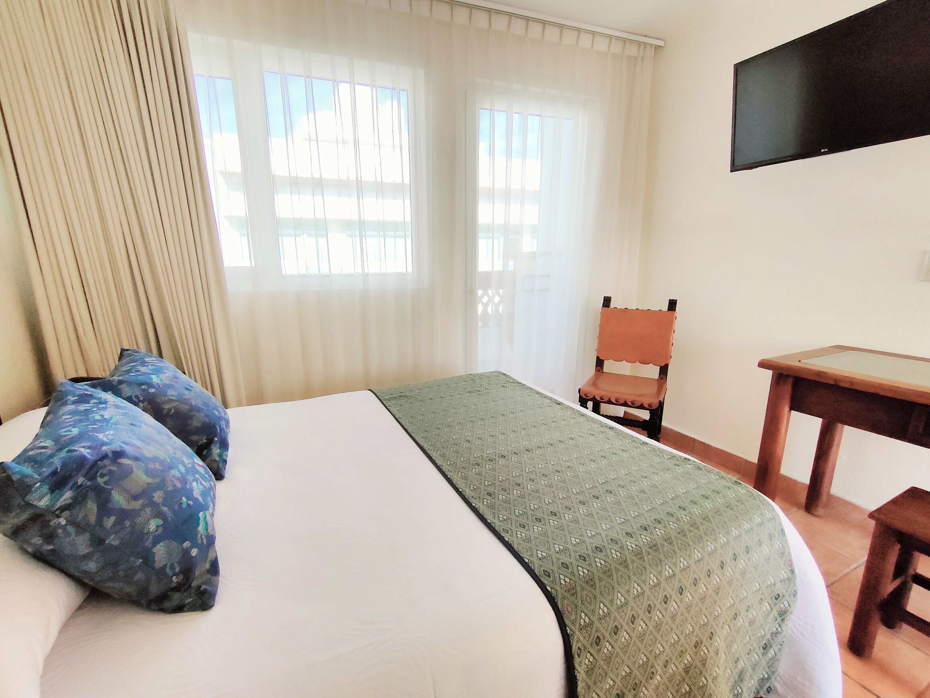 A hotel room with a bed, a desk, a chair, and a TV on the wall.