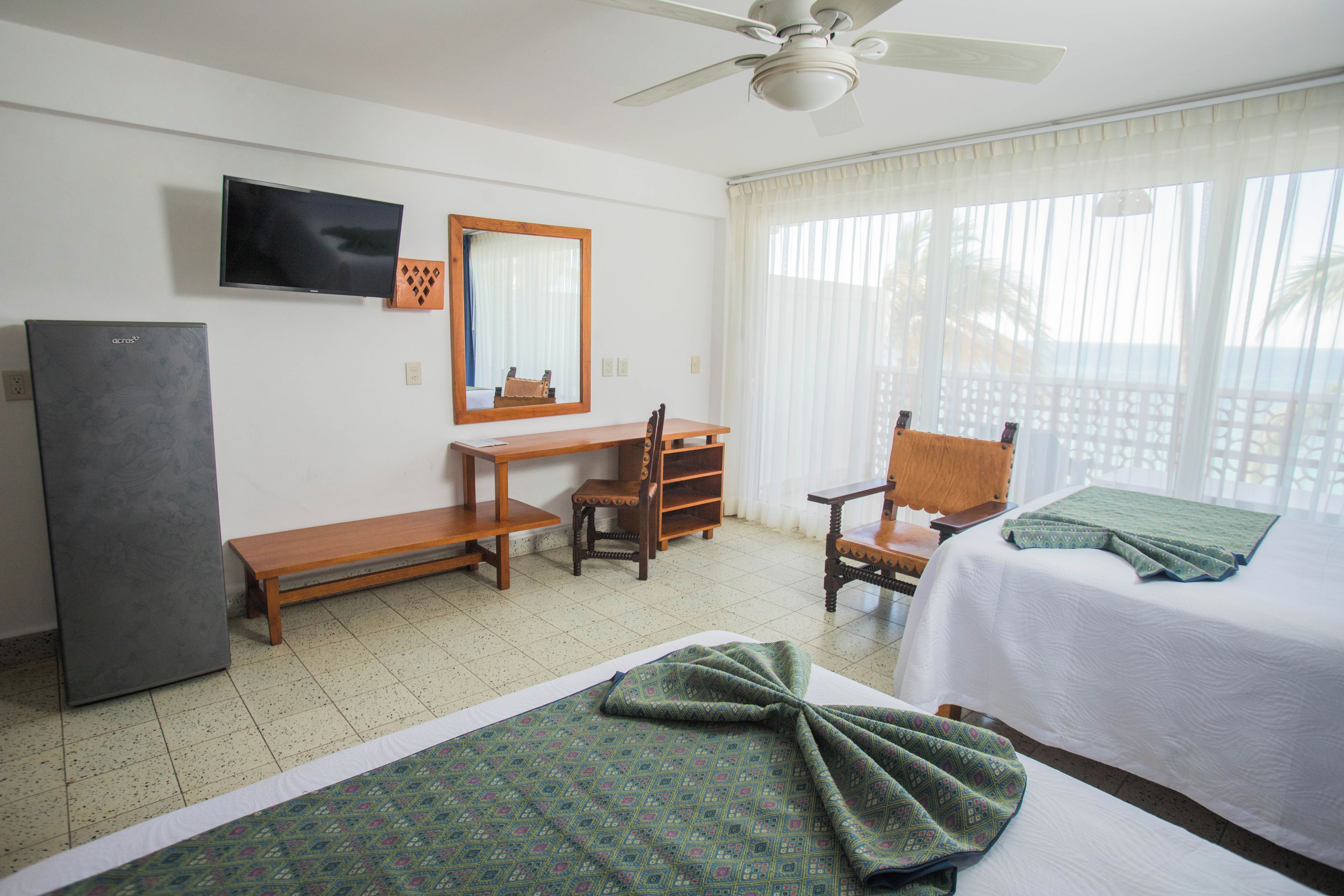 A hotel room with a bed, a desk, a chair, a television, and a ceiling fan.