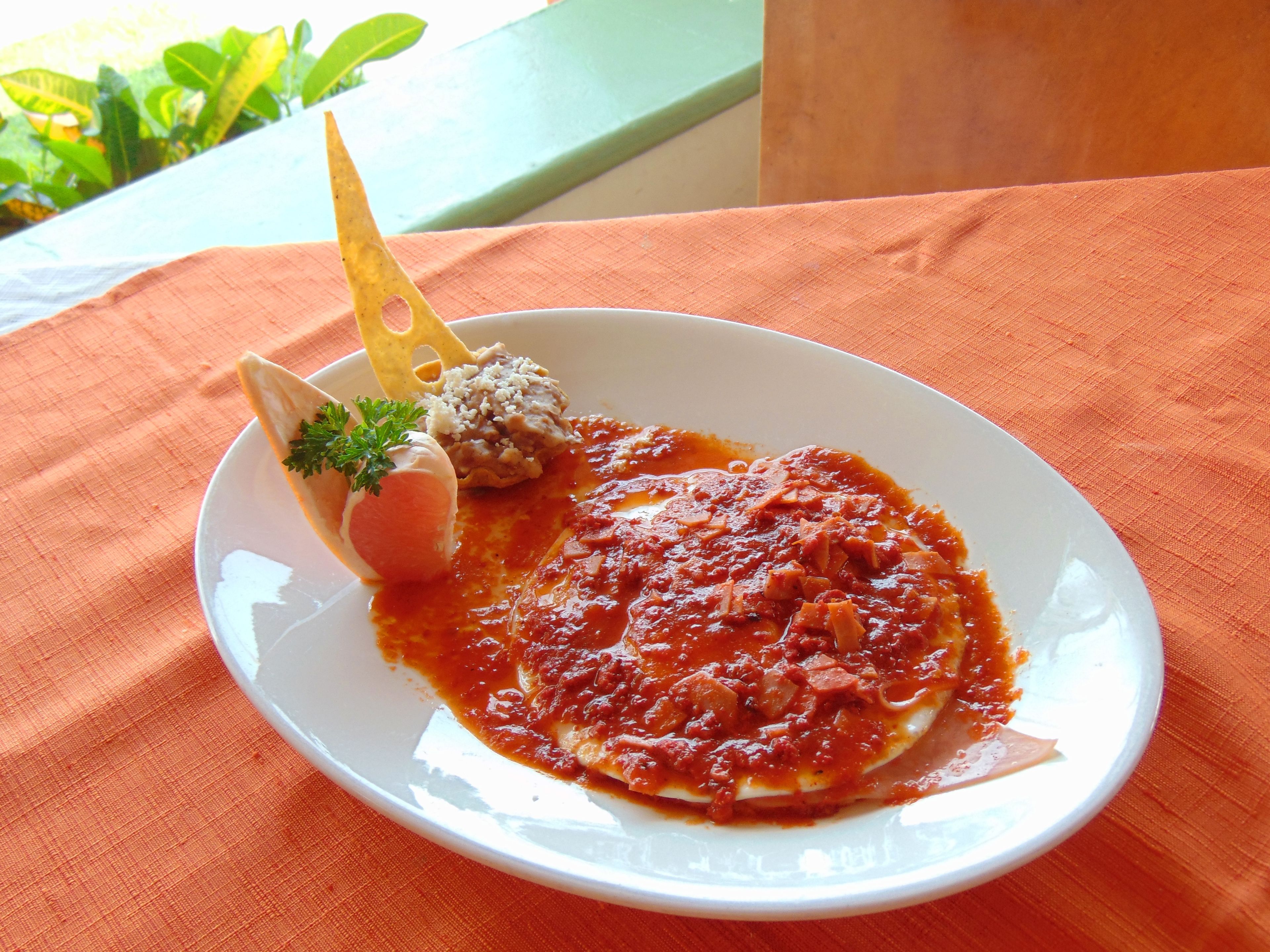A plate of food with a tomato-based sauce, a boiled egg, and a side of beans on a white plate.