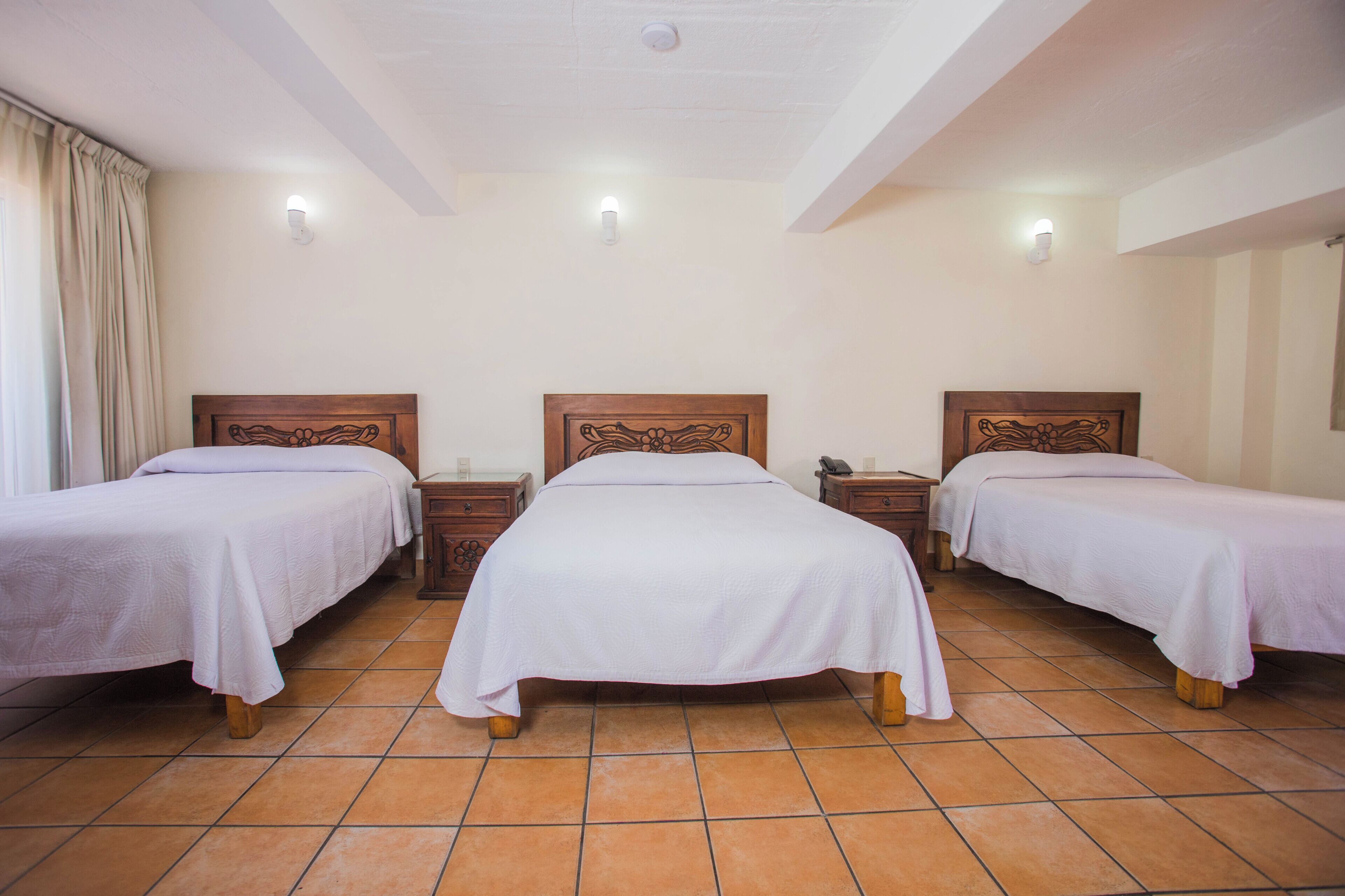 A hotel room with three single beds, a tiled floor, and a white ceiling.