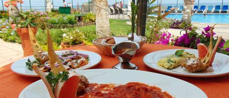 Una mesa con platos de comida, una piscina y vista al océano.