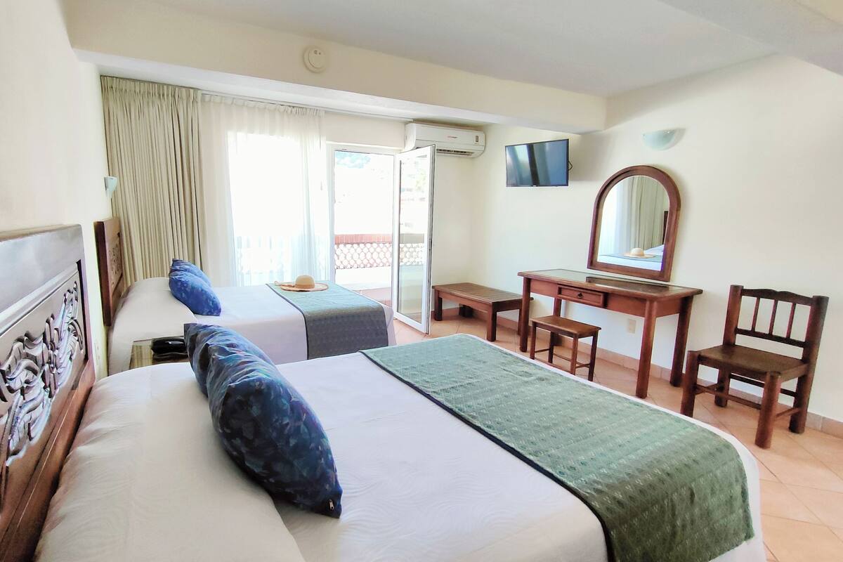 Ein Hotelzimmer mit Bett, Schreibtisch, Stuhl, Fernseher und einem Balkon mit Vorhängen.