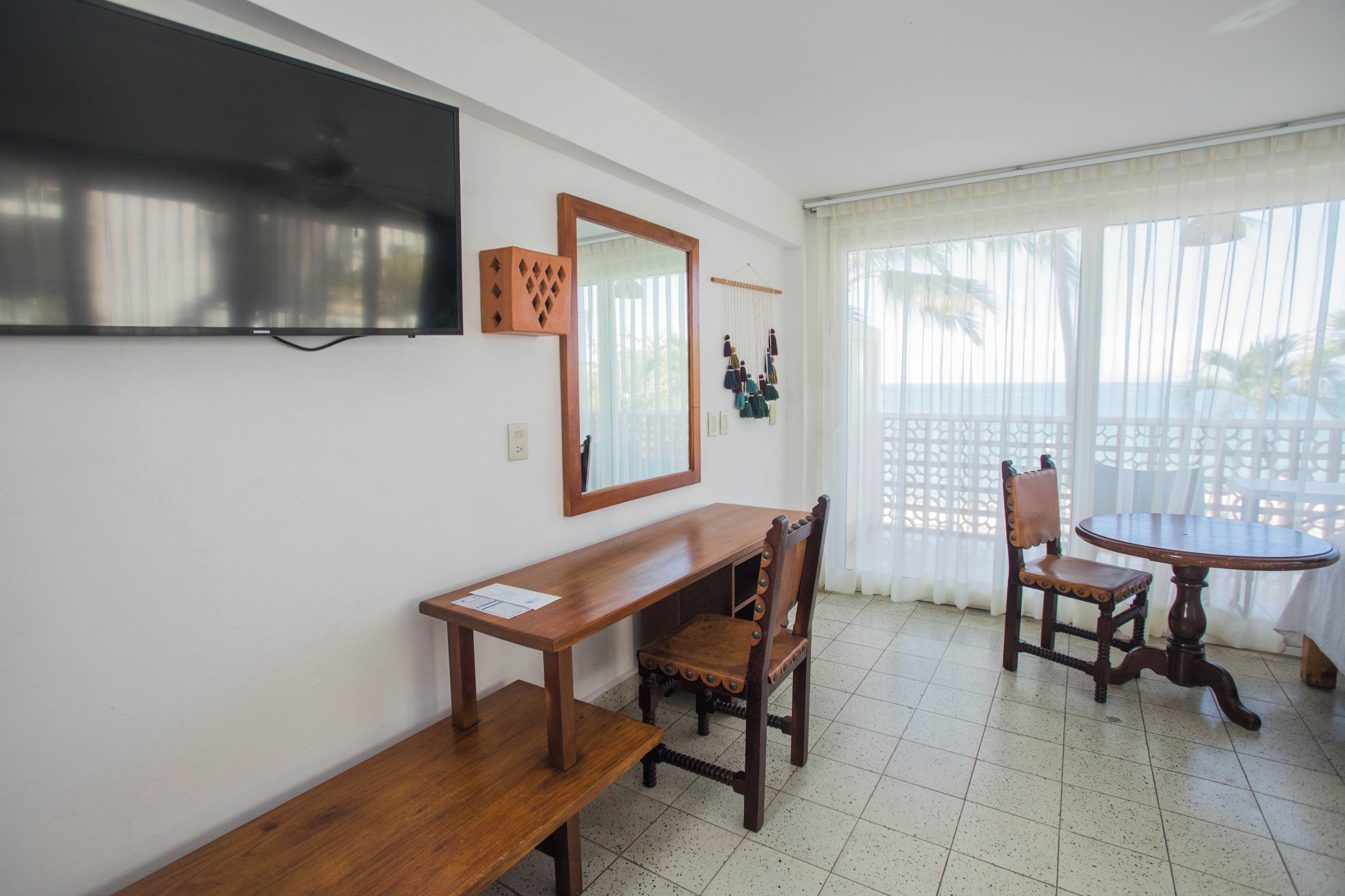 A room with a wooden table and chairs, a television mounted on the wall, and a window with a view of the outdoors.