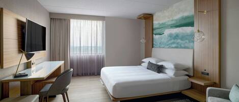 A modern hotel room with a large bed, a desk, a chair, a TV, and a painting on the wall.