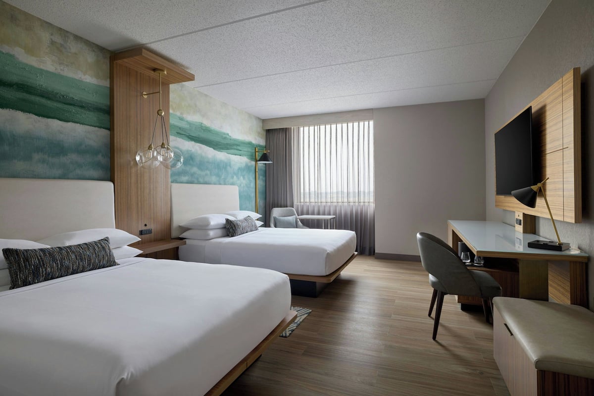 A hotel room with two beds, a desk, a chair, a TV, and a painting on the wall.