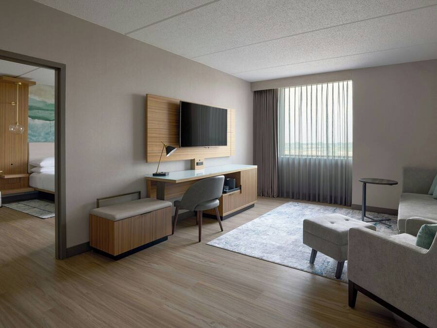 Ein modernes Hotelzimmer mit einem Holztisch, einem Flachbildfernseher, einer Sitzecke und einem großen Fenster mit Vorhängen.