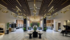 Un hall d’entrée spacieux, avec une grande table ronde au centre, un piano à queue et un lustre.