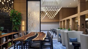 Un hall d’hôtel moderne avec une longue table de conférence en bois, des sièges confortables et un mur décoratif orné d’un motif géométrique.