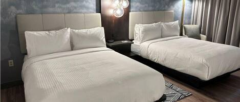 A hotel room with two beds, a modern chandelier, and a view of the ocean through the window.