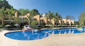 A resort with a large swimming pool, palm trees, and multiple buildings with balconies. - Hotel Rancho San Diego Grand Spa Resort (Ixtapan de la Sal)