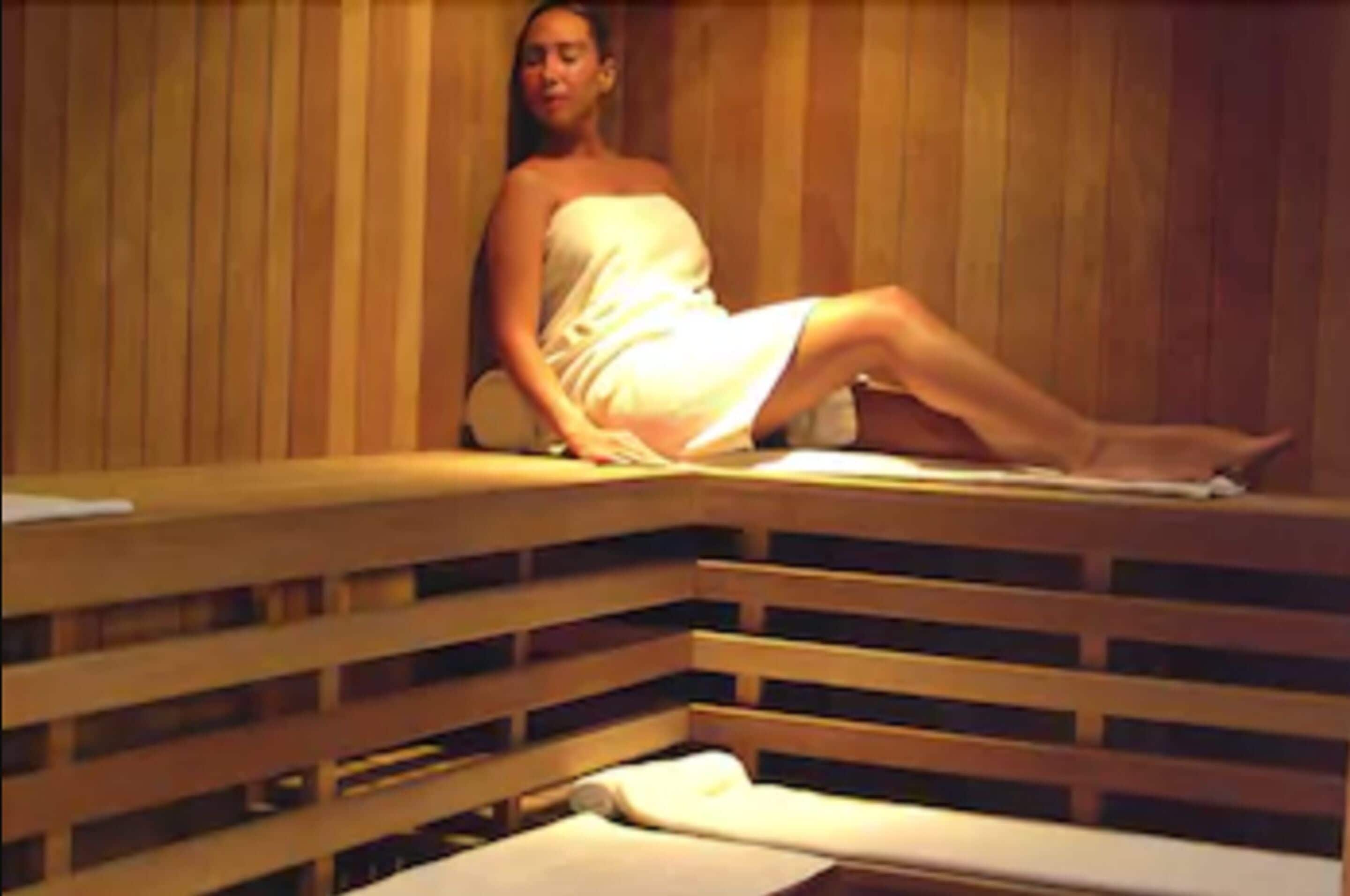 A person sitting in a wooden sauna with benches.