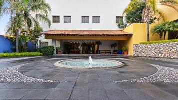Un hotel con una fuente central, un patio con baldosas y un edificio de techo a dos aguas y varias ventanas.