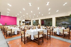 A banquet hall with multiple round tables and chairs, a bright pink wall, and a tiled floor.