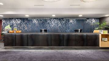 Un mostrador de recepción con superficie oscura, dos sillas y una pared decorativa con un diseño azul y blanco.