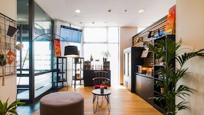 Un intérieur moderne avec un plancher en bois, un espace salon circulaire, une table à manger et un coin cuisine doté d’un meuble noir et d’une plante.