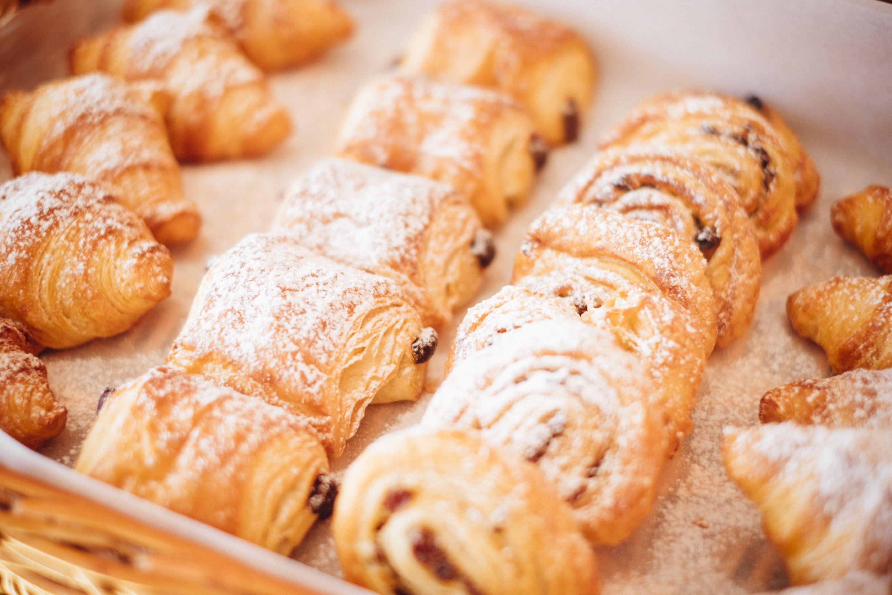Una bandeja con varios pasteles, incluyendo croissants y rollos de canela, espolvoreados con azúcar glas.