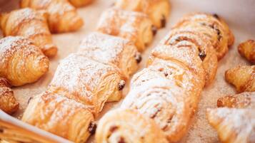 Un plateau rempli d’une variété de viennoiseries, notamment des croissants et des pains aux cannelle, saupoudrés de sucre glace.