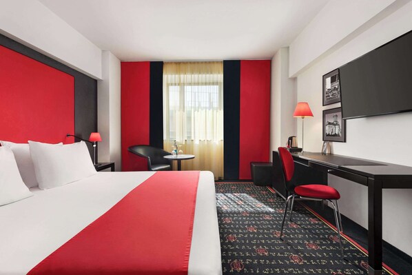 A hotel room with a large bed, a desk with a chair, a small table with a chair, and a TV mounted on the wall.